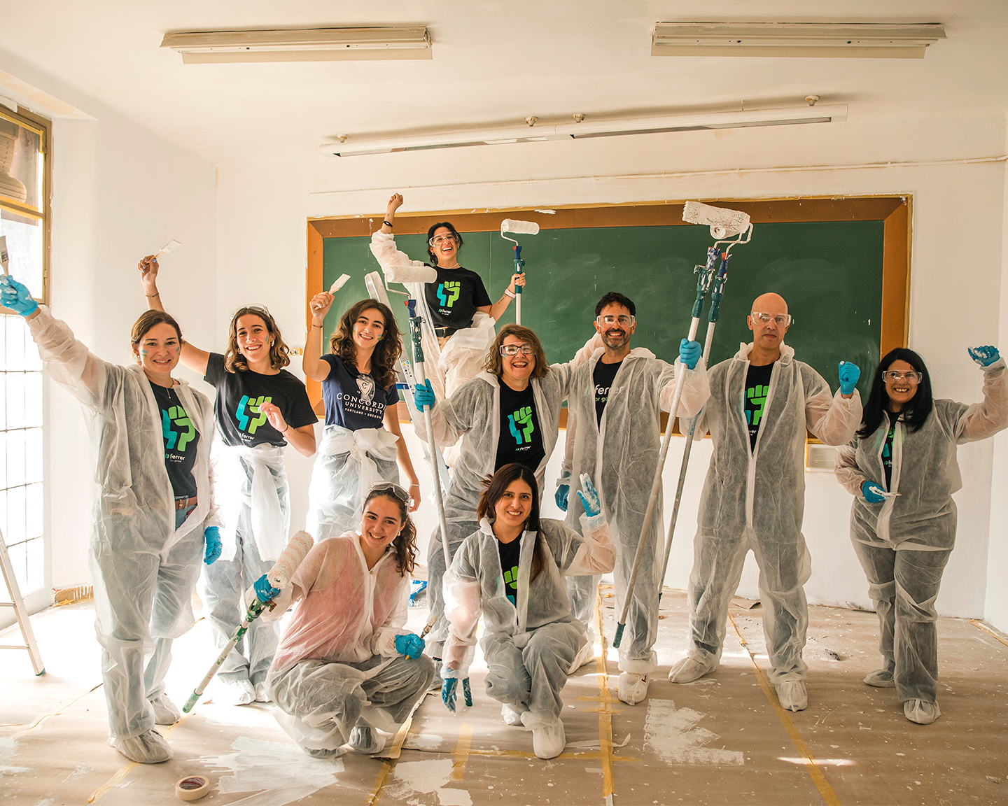 Grup de voluntaris en una iniciativa d'acció col·lectiva, equipats amb granotes protectores i rodets per pintar una aula escolar amb Grup Ferrer.