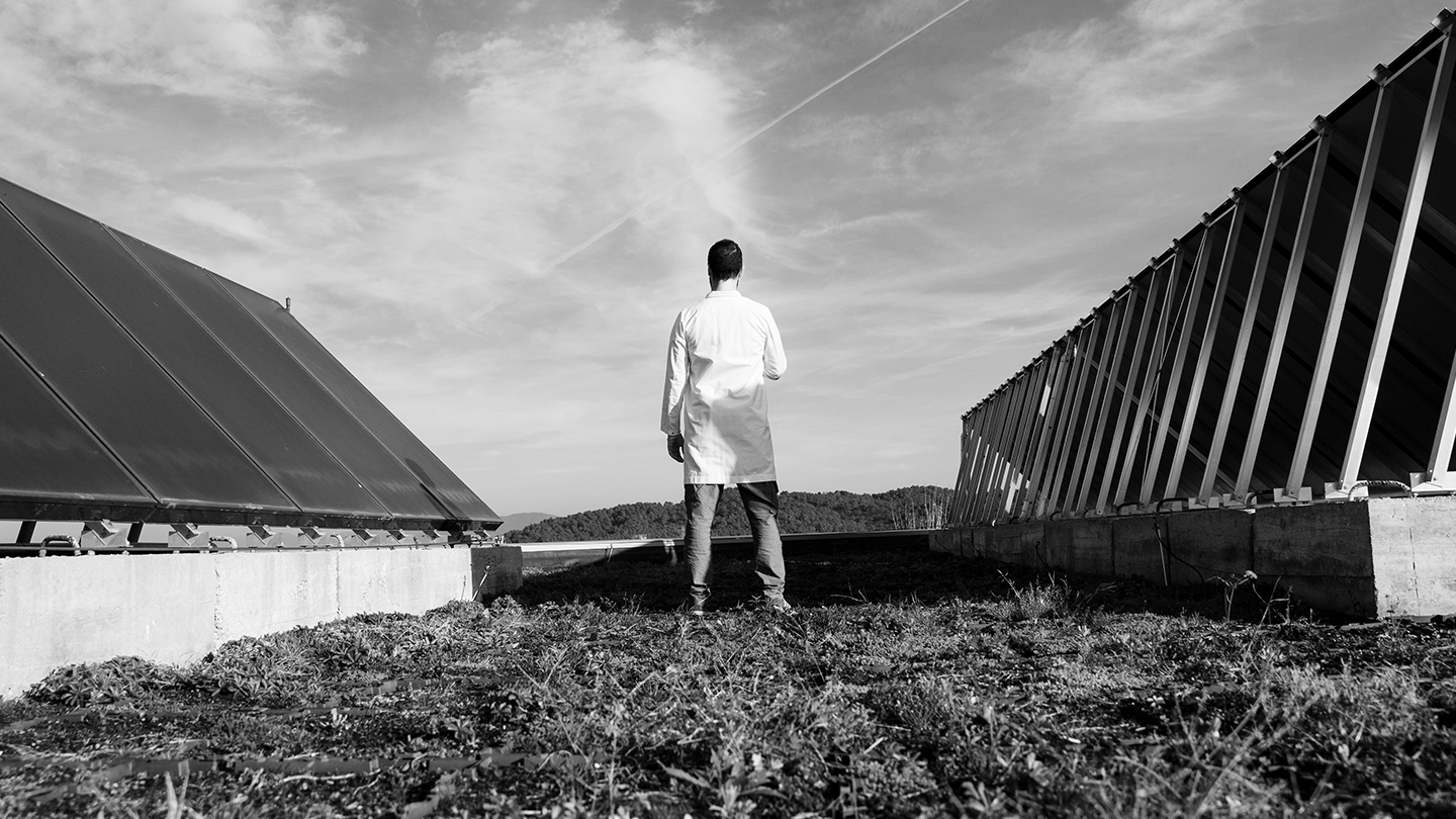 A professional in a white coat observing an installation of solar panels on a plant soil at the Ferrer company.