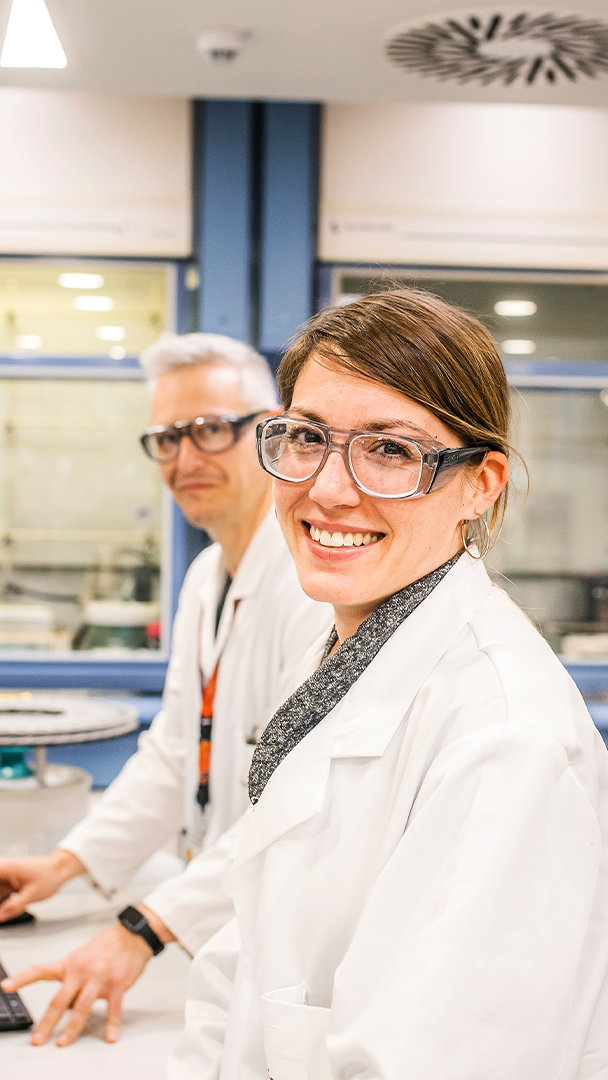 Profesionales de Ferrer en un laboratorio, vestidos con bata blanca y sonriendo a cámara en un entorno de investigación.