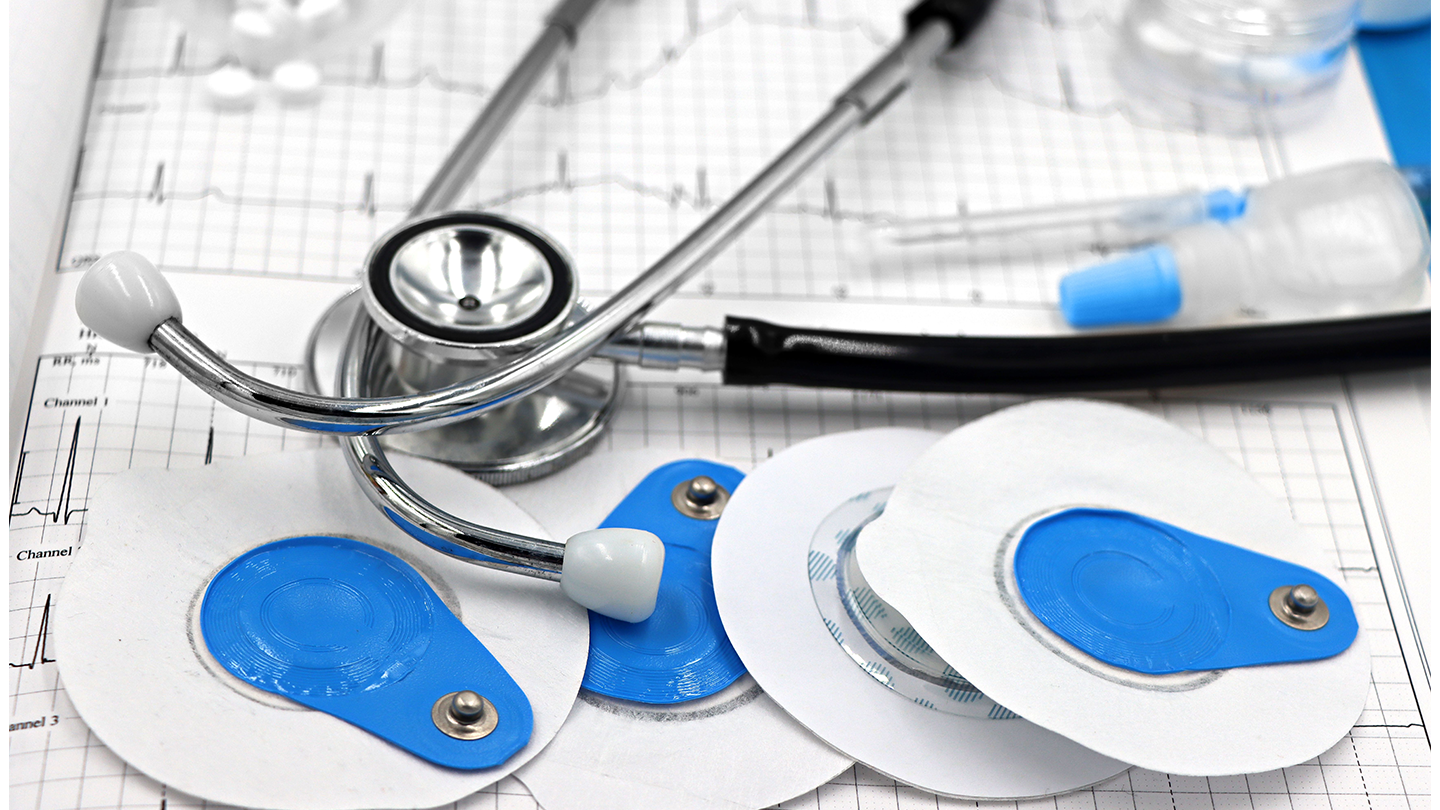 Un estetoscopio y varios electrodos de electrocardiograma de color azul y blanco reposan sobre un informe médico impreso.