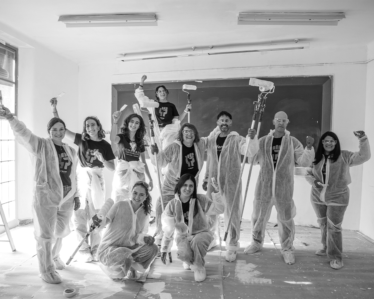 Grupo de voluntarios en una iniciativa de acción colectiva, equipados con monos protectores y rodillos para pintar un aula escolar con Grupo Ferrer.