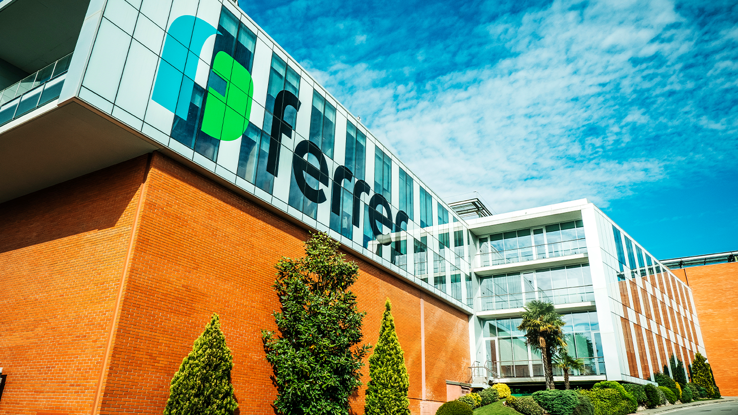 Vista en angle contrapicat de l' exterior d' un edifici corporatiu modern amb el logotip i inscripció de Ferrer a la façana sota un cel blau amb núvols.