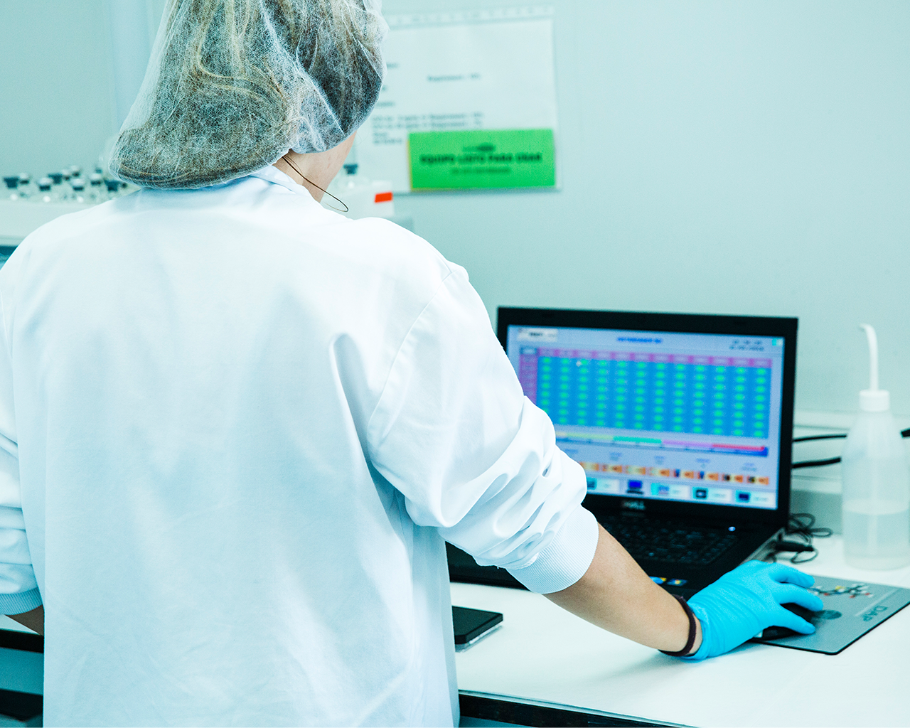 A laboratory technician in a white coat and gloves analysing data on a computer at the Ferrer company's facilities.
