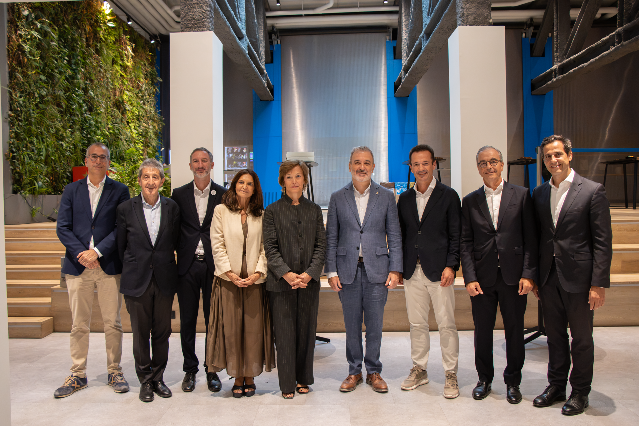 Grupo de ocho profesionales posando alineados en un espacio moderno de techos altos con un jardín vertical al fondo.