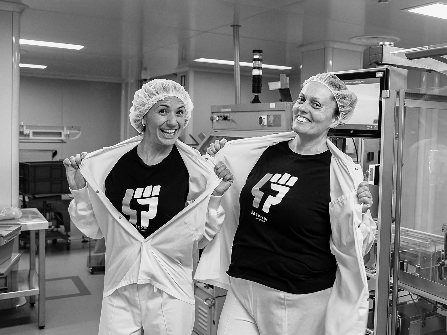 Dos empleadas de Grupo Ferrer mostrando su camiseta corporativa en la planta de producción.