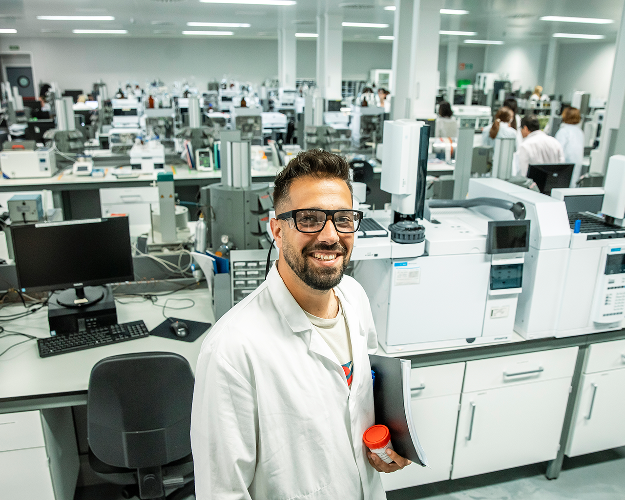 Professional de Ferrer somrint a càmera en un laboratori, envoltat d' equips d' anàlisi i tecnologia científica.