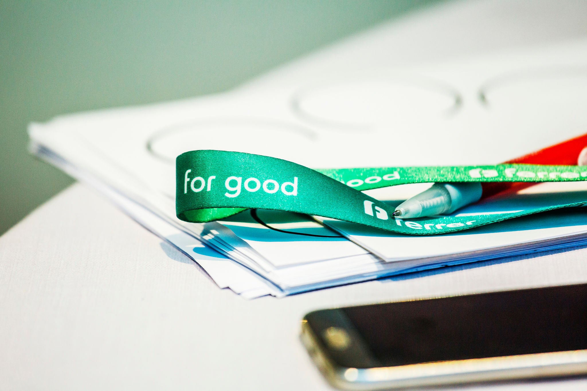 Detalle de una mesa de trabajo con documentos, un móvil y una cinta verde de Ferrer con el mensaje “Ferrer for good”.