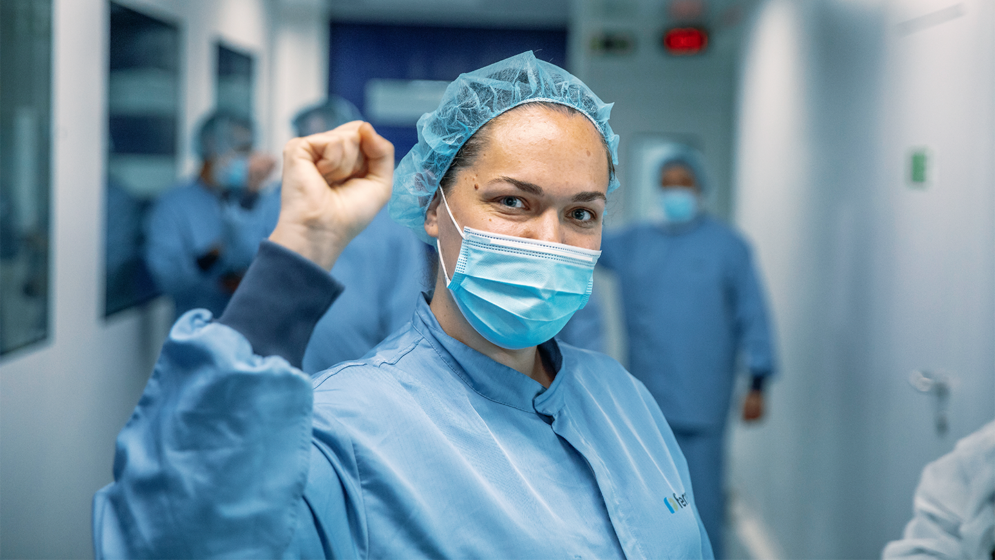 Employee of Grupo Ferrer wearing a mask and sanitary uniform celebrating the success of the team in the pharmaceutical laboratory.
