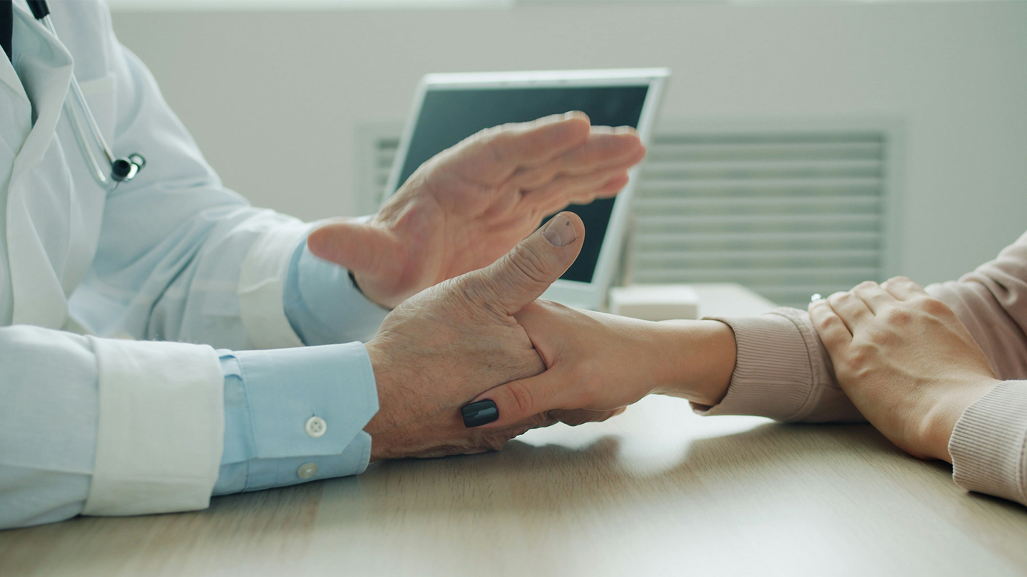 Primer plano de un médico sosteniendo la mano de una paciente en la consulta, reflejando el compromiso con la salud de la empresa Ferrer.