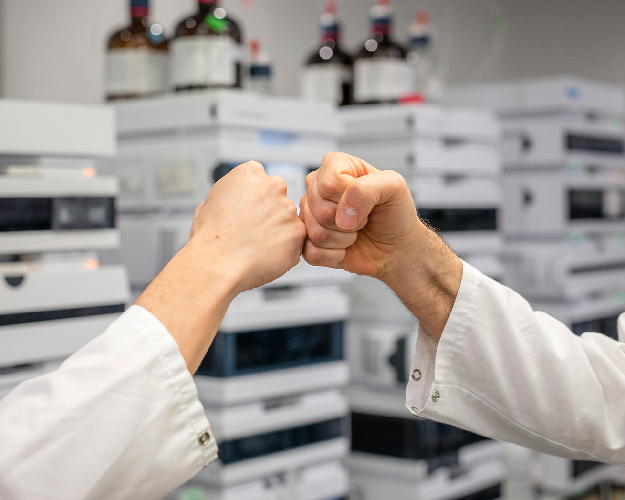 Científicos chocando los puños en un laboratorio de investigación, simbolizando el éxito en un acuerdo de colaboración con el departamento de desarrollo de negocio de Ferrer.