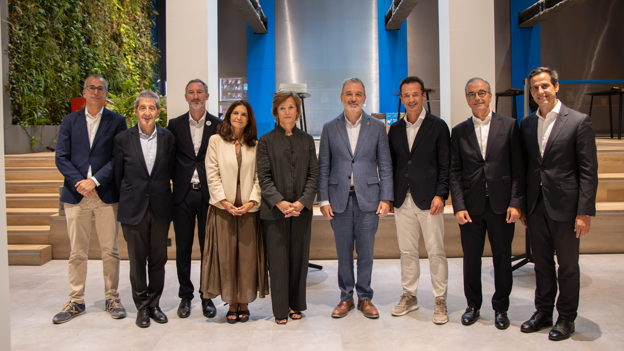 Grup de vuit professionals posant alineats en un espai modern de sostres alts amb un jardí vertical al fons.