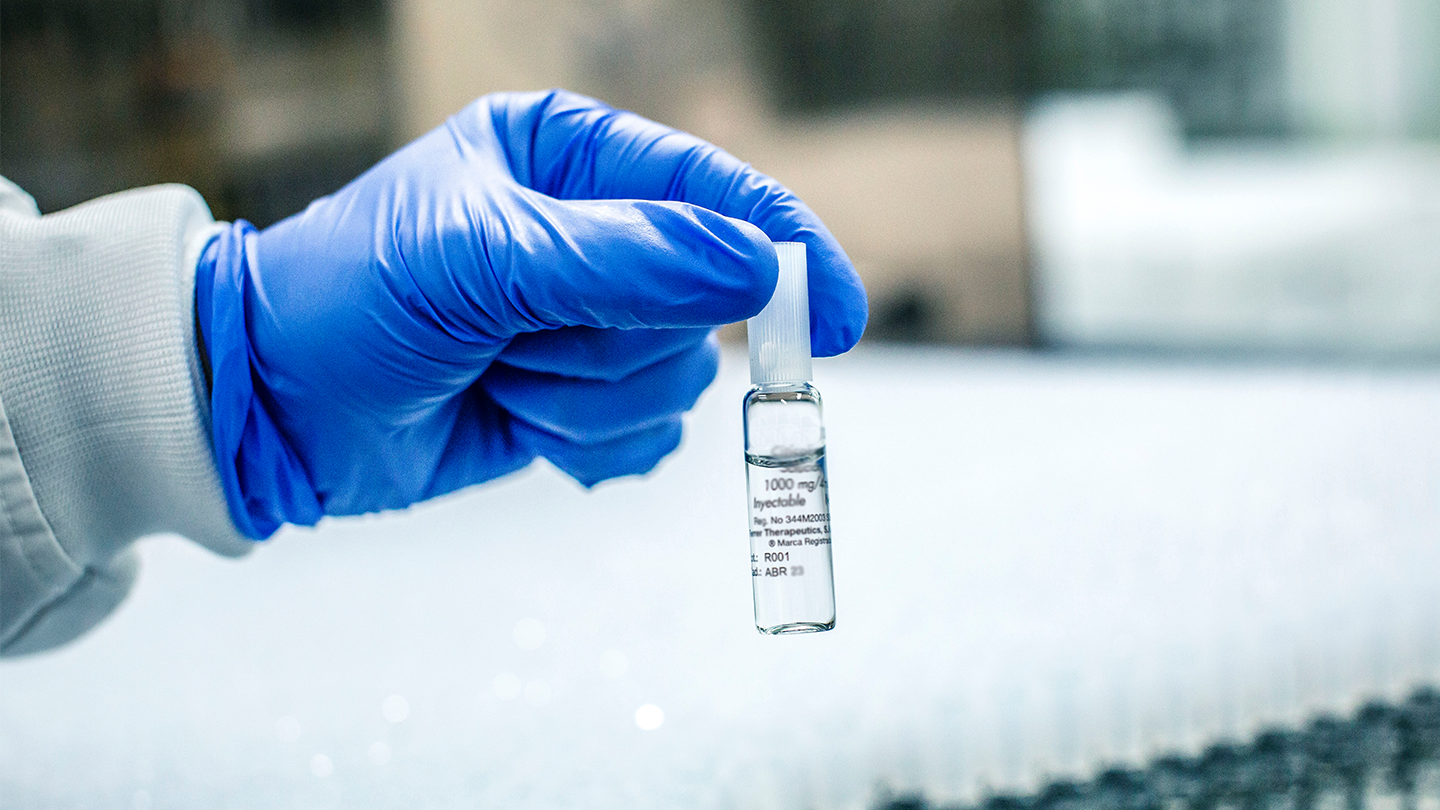 Primer plano de una mano con guante azul sosteniendo una ampolla de medicamento inyectable en la planta de producción de Ferrer.