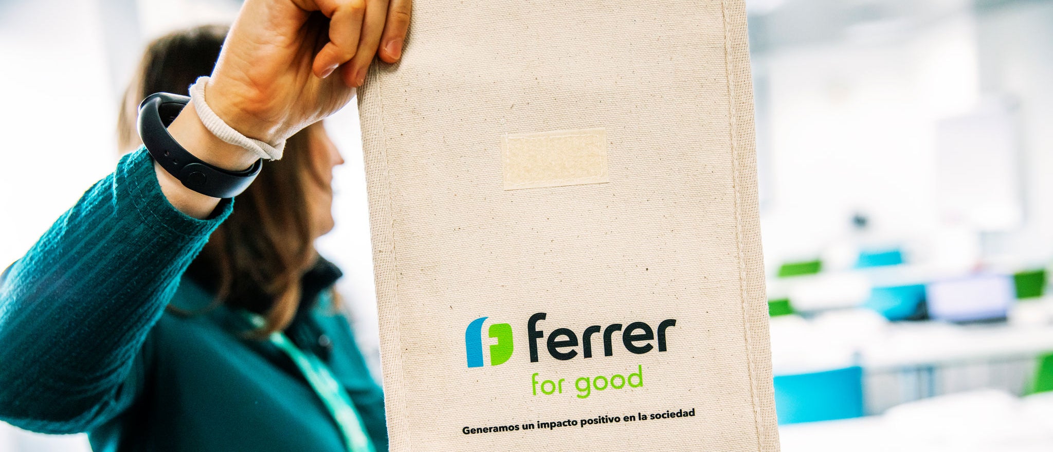 Persona sostiene una bolsa reutilizable de tela con el logo “Ferrer for Good” en un espacio interior luminoso, relacionado con una actividad corporativa o de voluntariado de Ferrer.