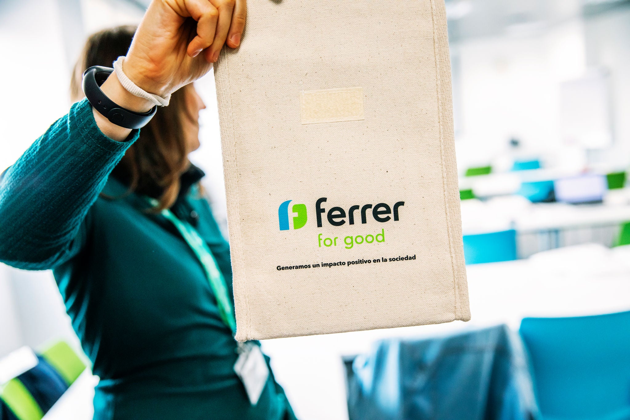 Persona sostiene una bolsa reutilizable de tela con el logo “Ferrer for Good” en un espacio interior luminoso, relacionado con una actividad corporativa o de voluntariado de Ferrer.
