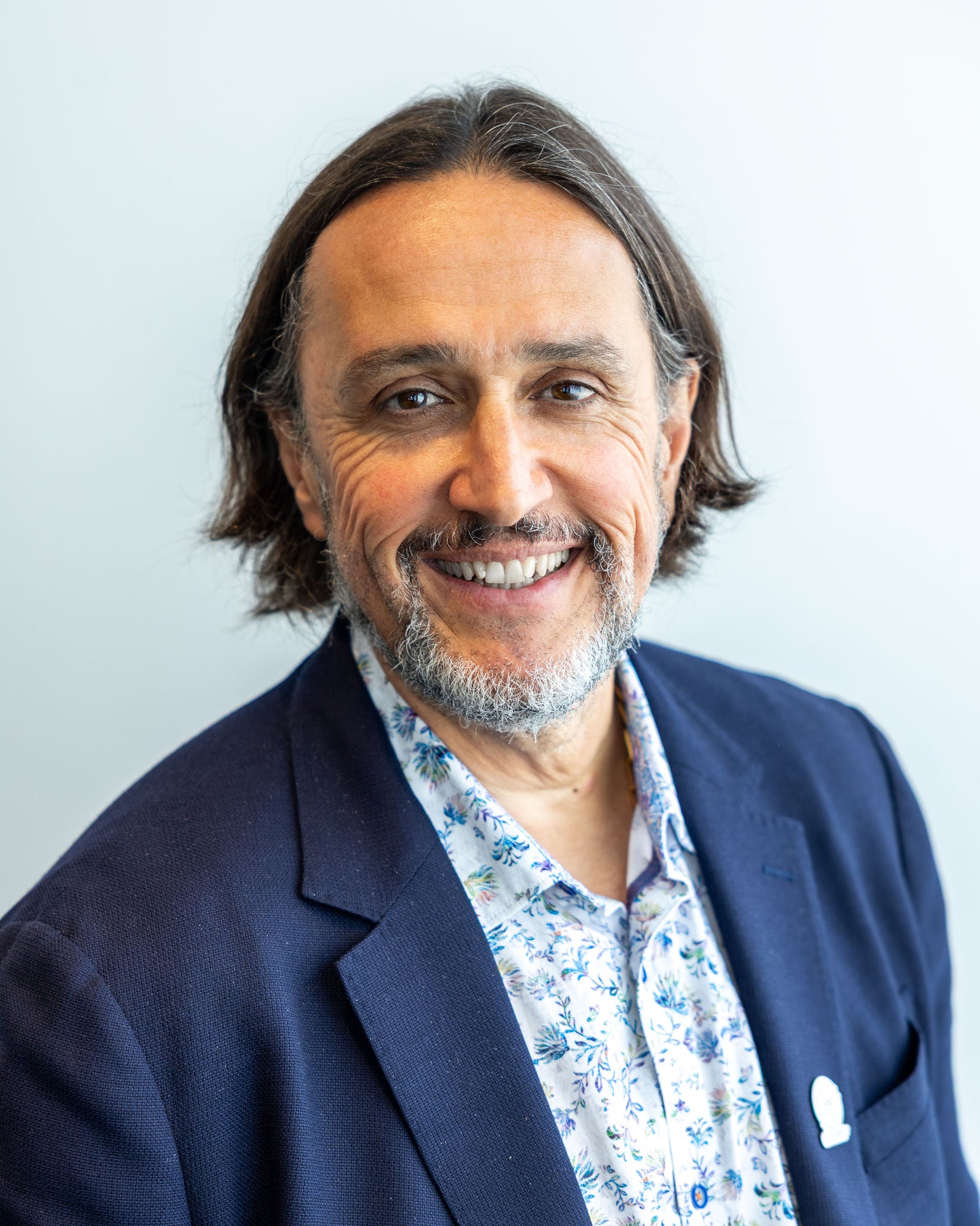 Retrato corporativo de un profesional de Ferrer sonriendo a cámara, vestido con americana azul y camisa estampada sobre fondo claro.
