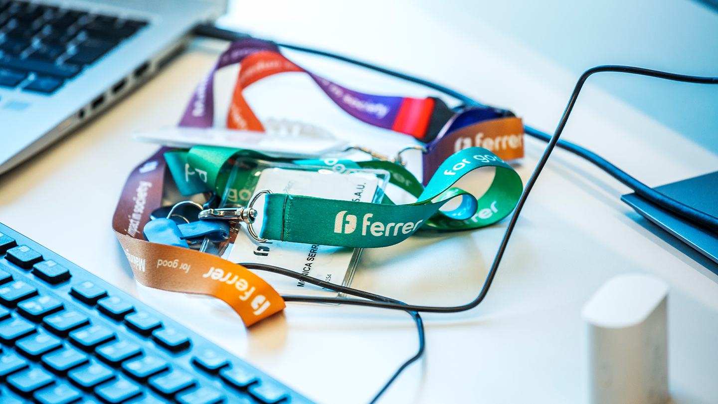 Acreditacions i lanyards de colors amb el logotip de l' empresa Ferrer sobre un escriptori d' oficina.