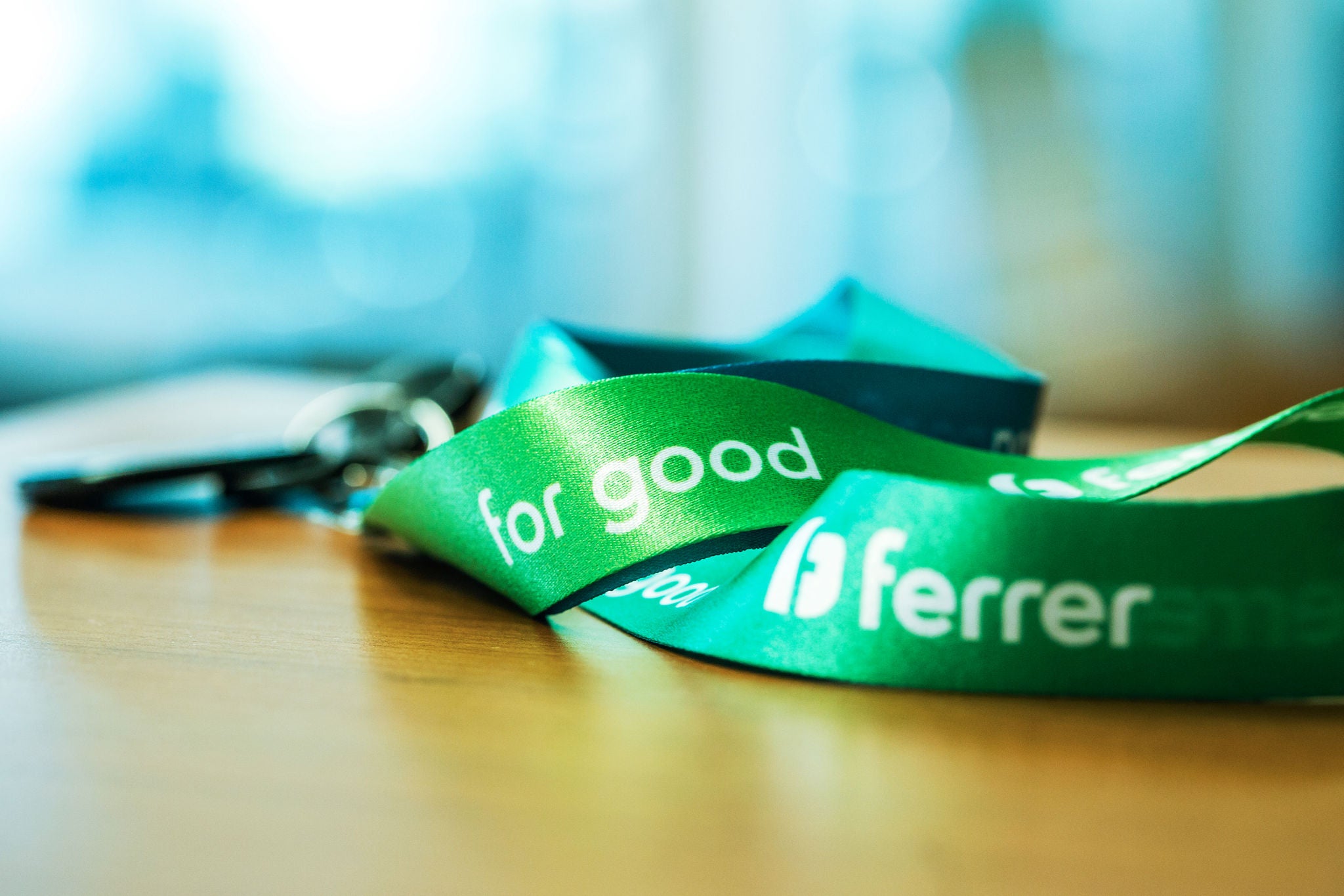 Ferrer's corporate green ribbon on a wooden table, with the slogan "for good" in the foreground and the background blurred.