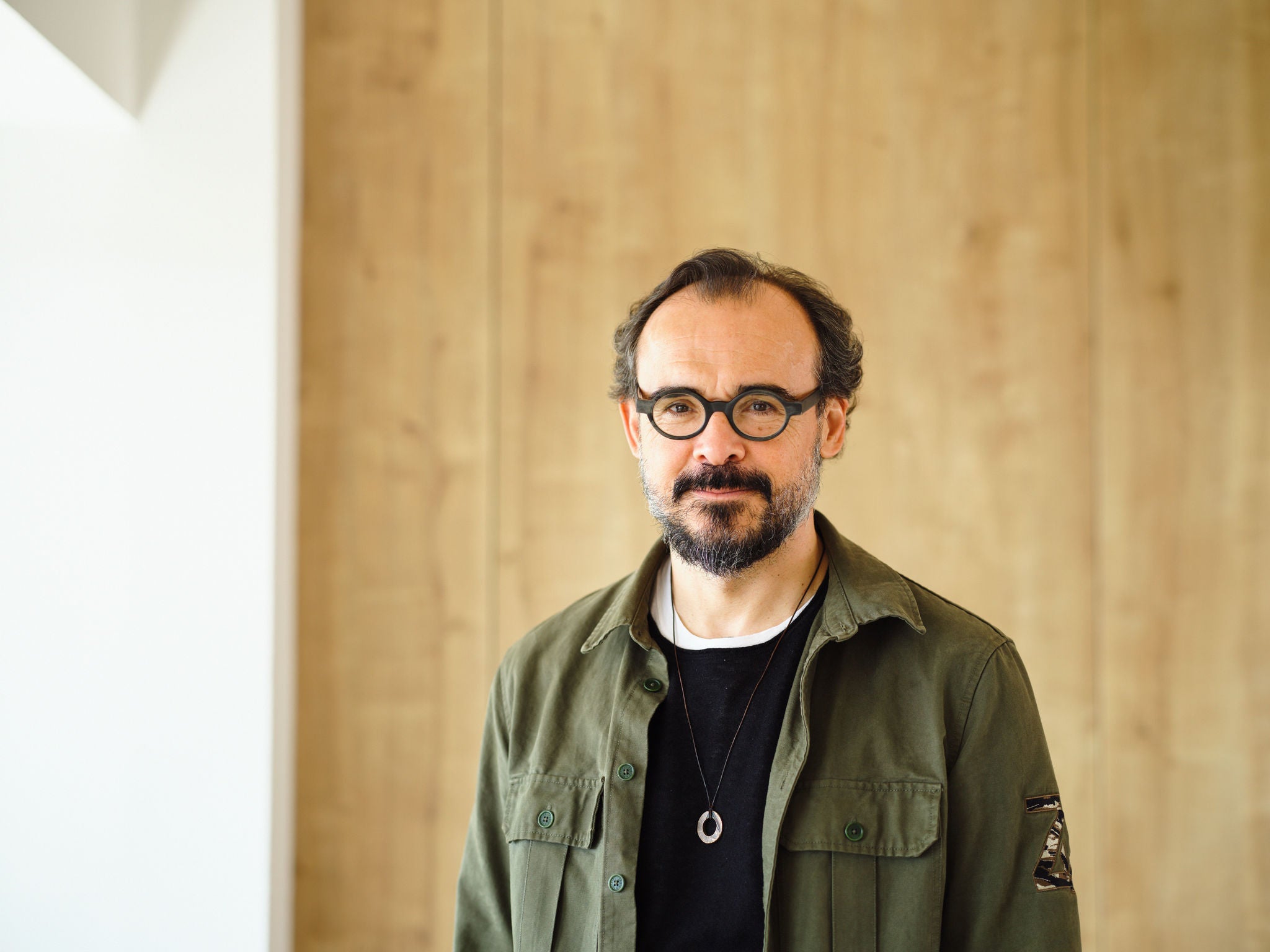 Retrato de Sergi Ferrer-Salat, con gafas, barba y camisa verde, posando frente a una pared de madera clara.