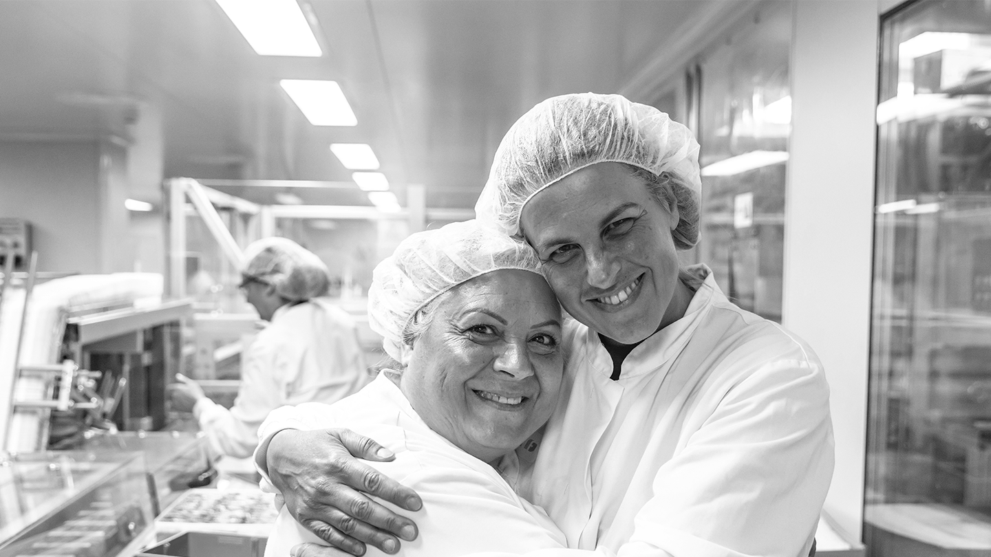 Dues operàries de laboratori de l'empresa Ferrer somrien mentre s'abracen a la planta de producció.