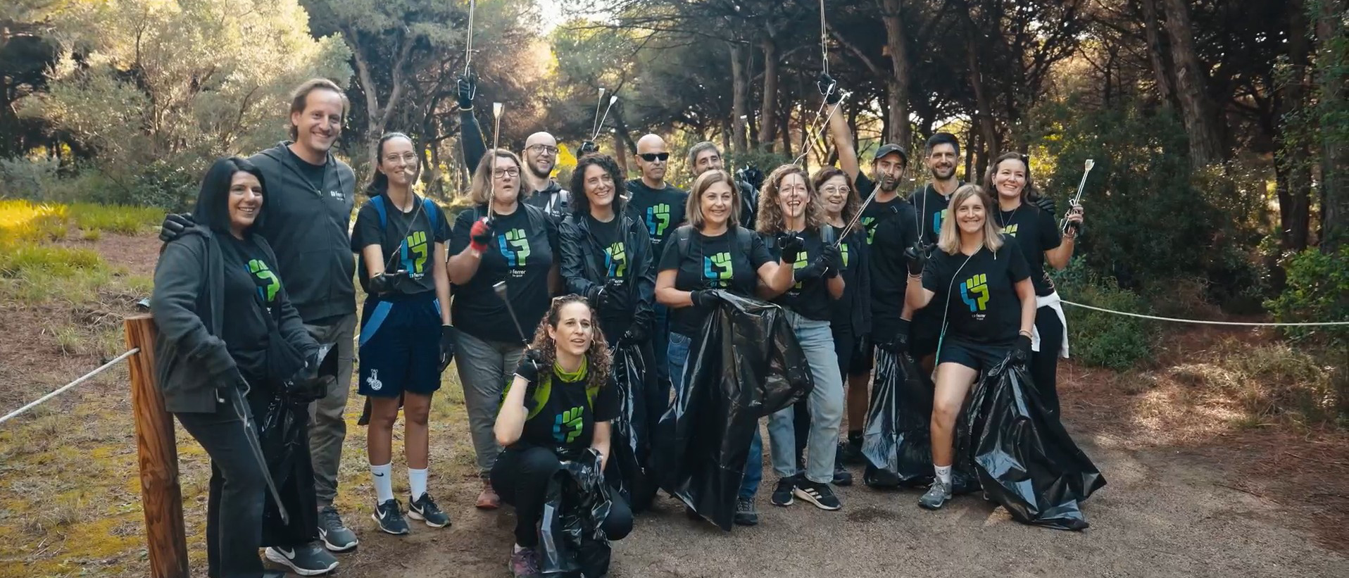 Grupo de voluntarias de Ferrer en un entorno natural, sonriendo a cámara durante una actividad de limpieza y recogida de residuos, con bolsas y guantes.