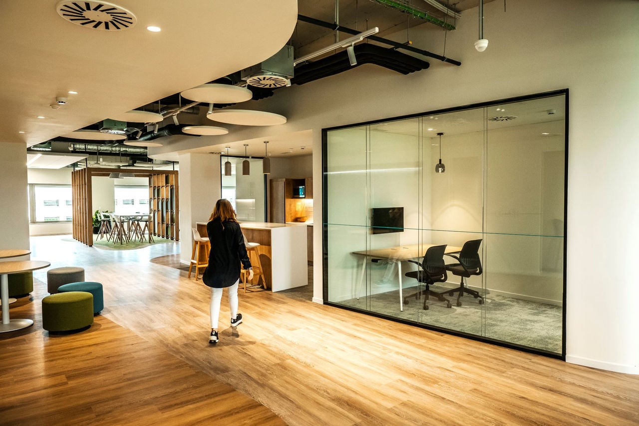 Person walking through a modern and bright office, with glass rooms, common areas and designer furniture.