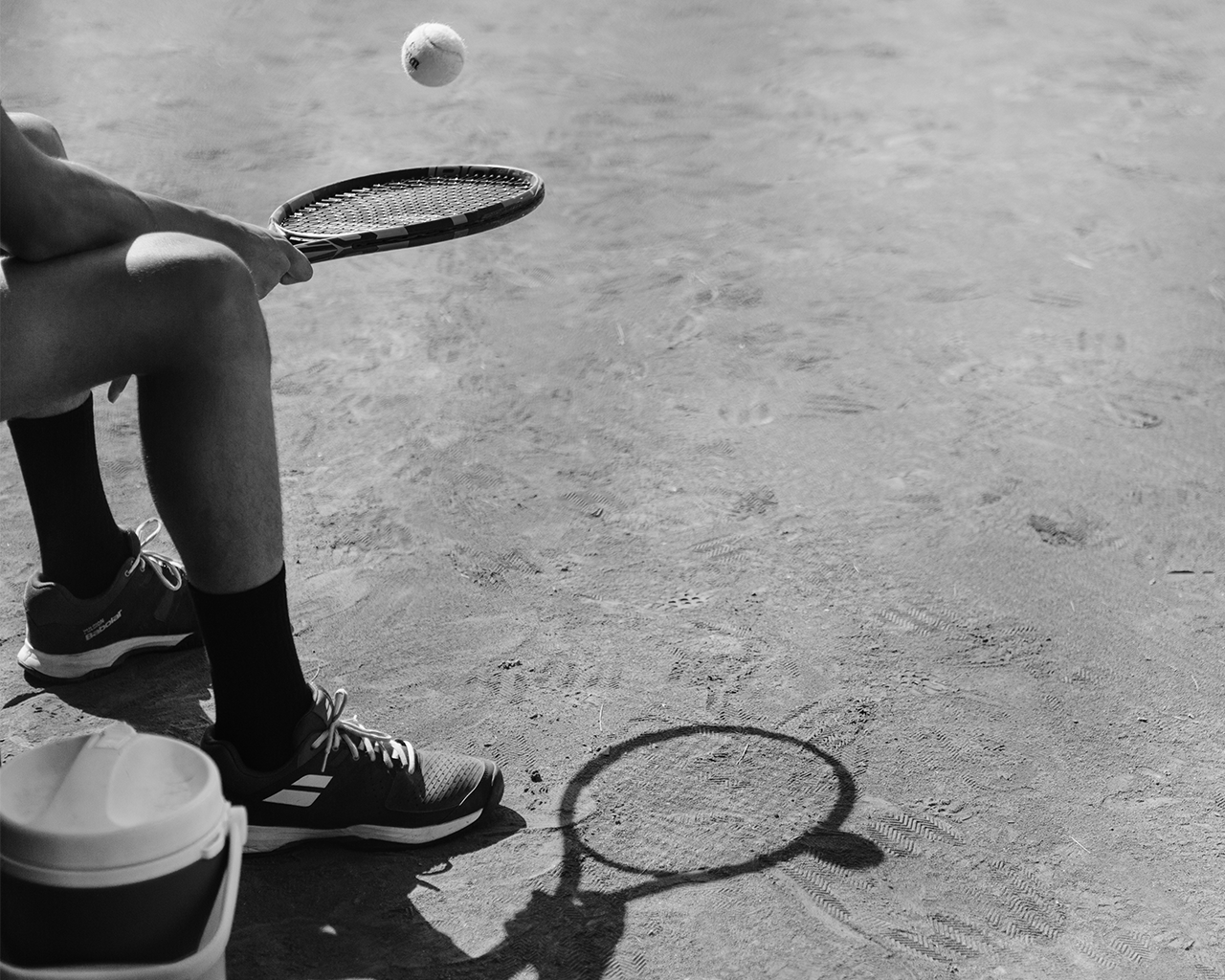 A tennis player sits with his racket and a ball in the air on a clay court, during a talent promotion program of the Ferrer Foundation.