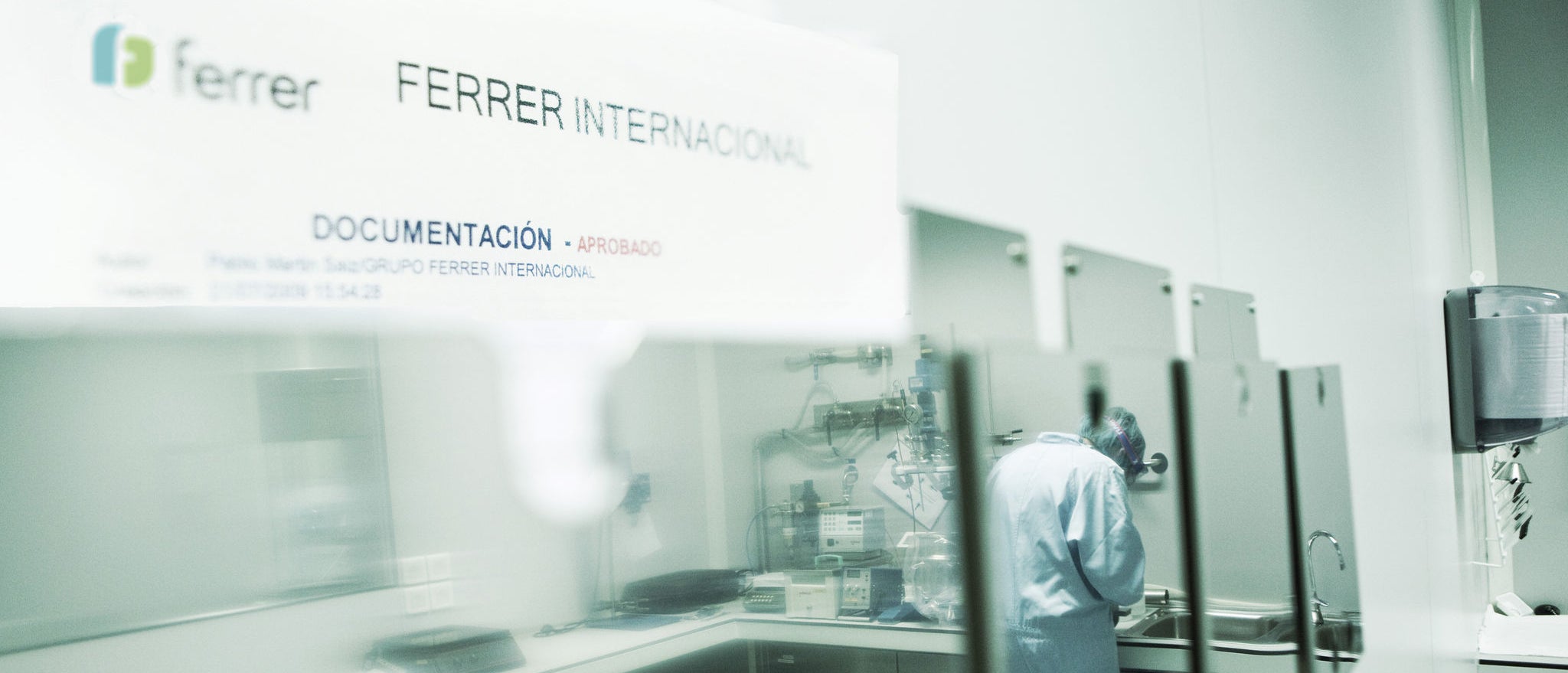 Vista d'una àrea de documentació en instal·lacions de Ferrer Internacional, amb una persona treballant en un entorn tècnic o de laboratori després d'una zona envidrada.
