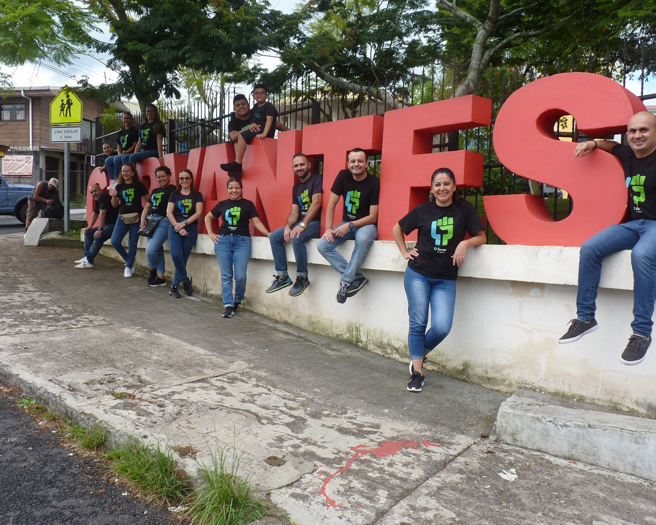 Equipo de Ferrer posa sonriendo junto a un rótulo exterior, vistiendo camisetas corporativas durante una actividad de voluntariado o colaboración social.