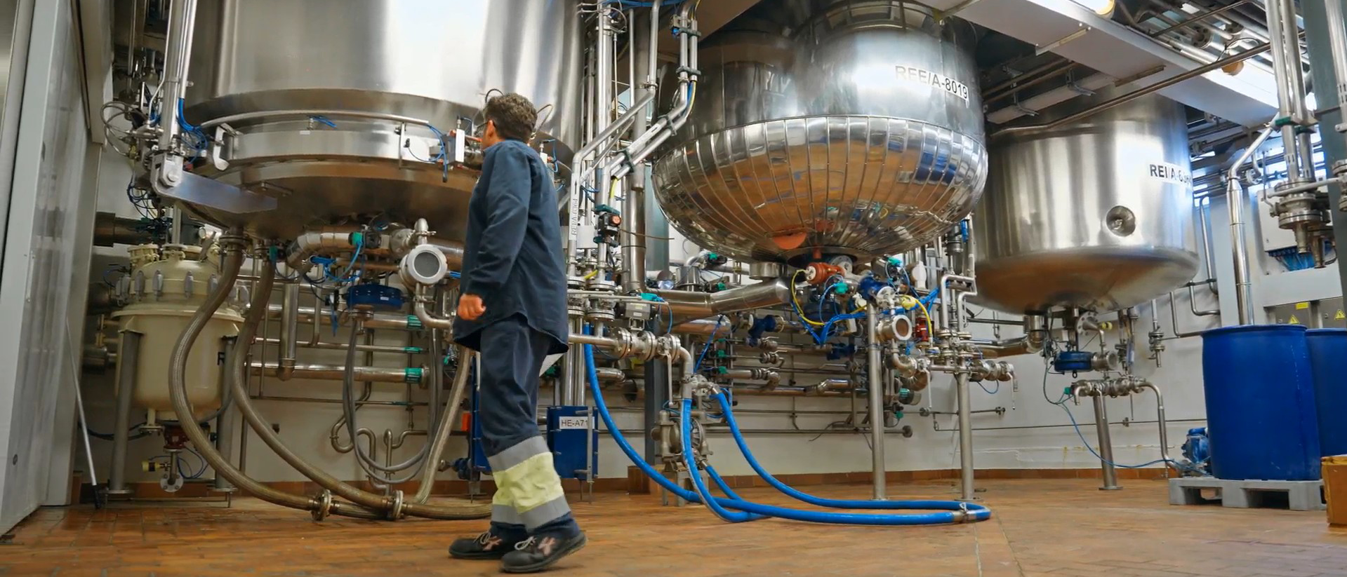 Profesional de Ferrer en una zona de producción industrial, caminando junto a equipos y depósitos metálicos.