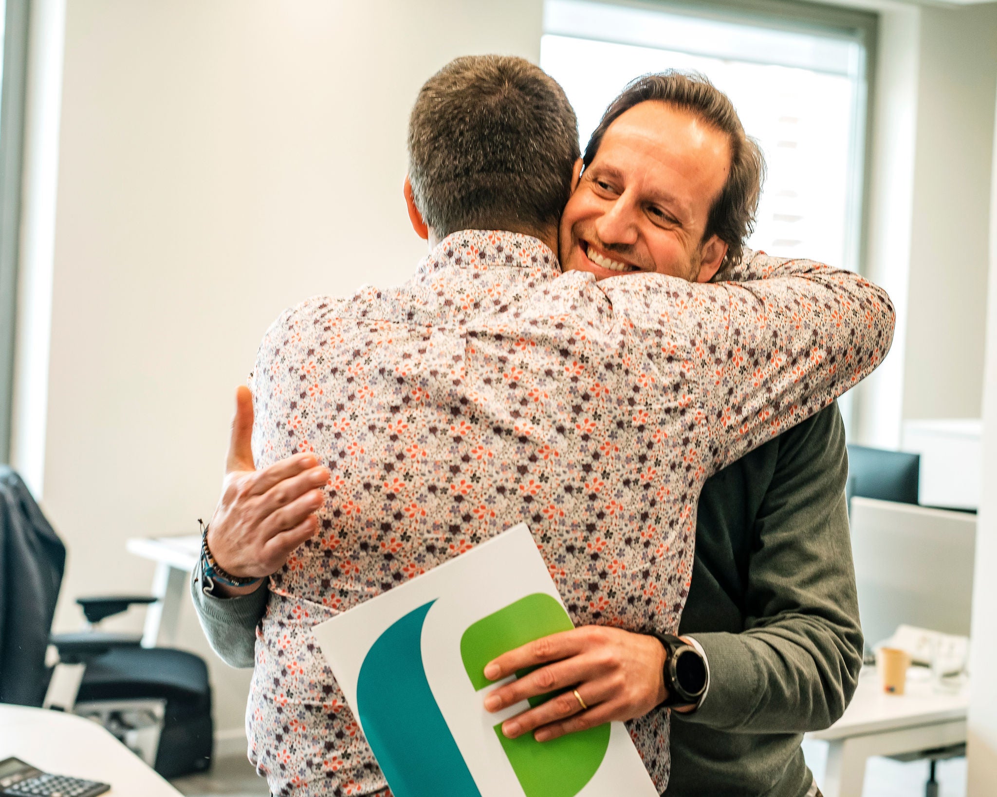 Dos professionals de Ferrer s'abracen en un entorn d'oficina, transmetent rodalia, reconeixement i esperit d'equip.