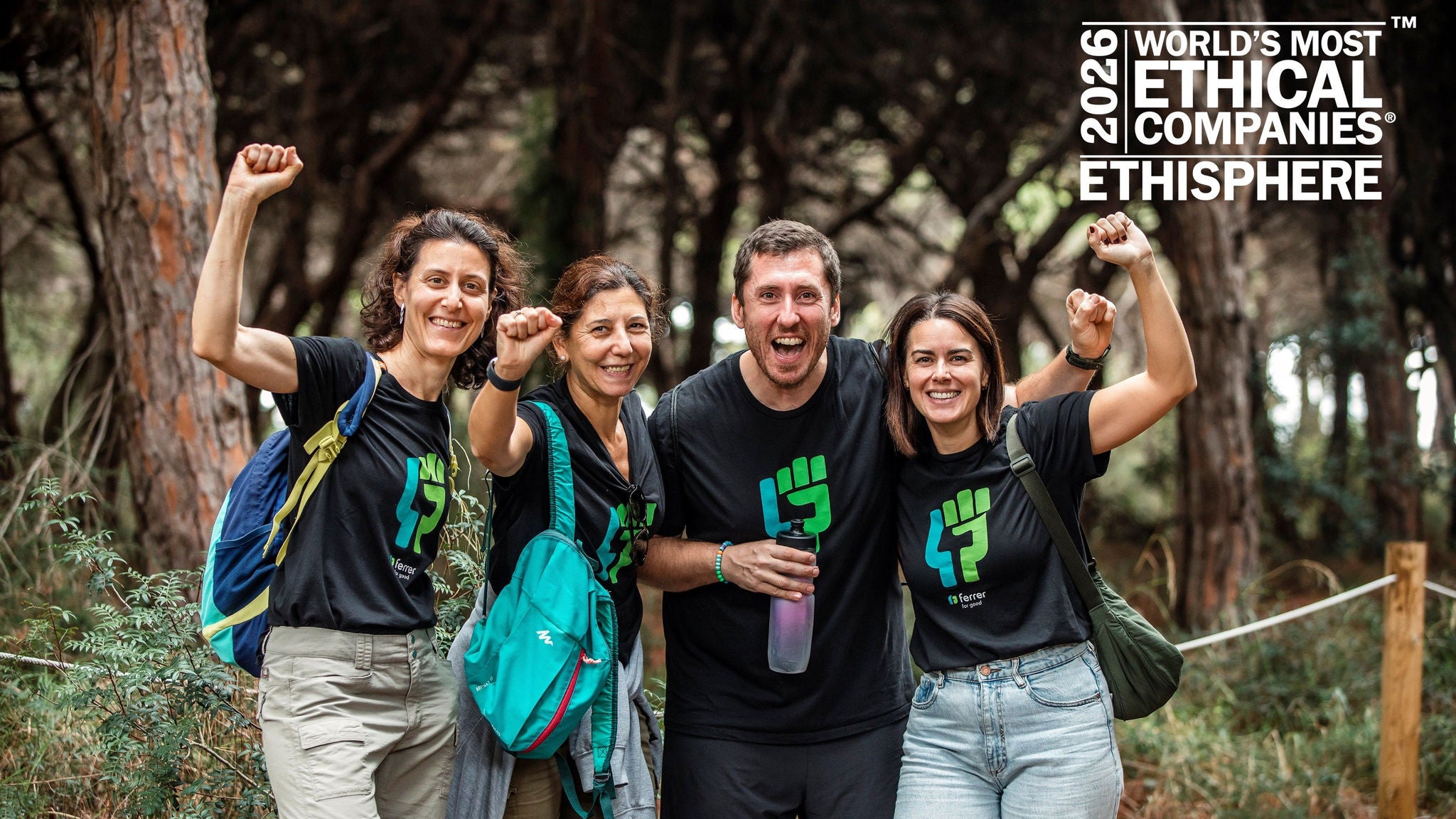 Cuatro personas sonrientes con camisetas a juego celebrando en un bosque con los puños en alto.