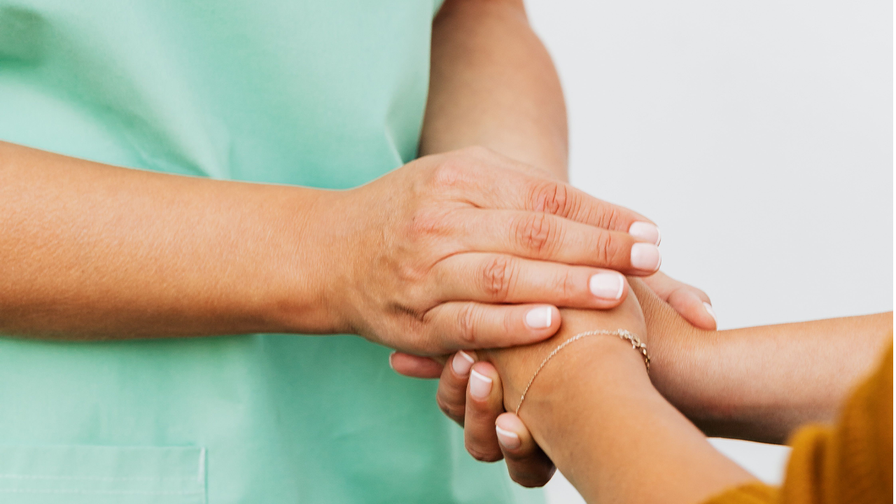 Close-up of a health professional in green uniform empathetically holding a patient's hand.