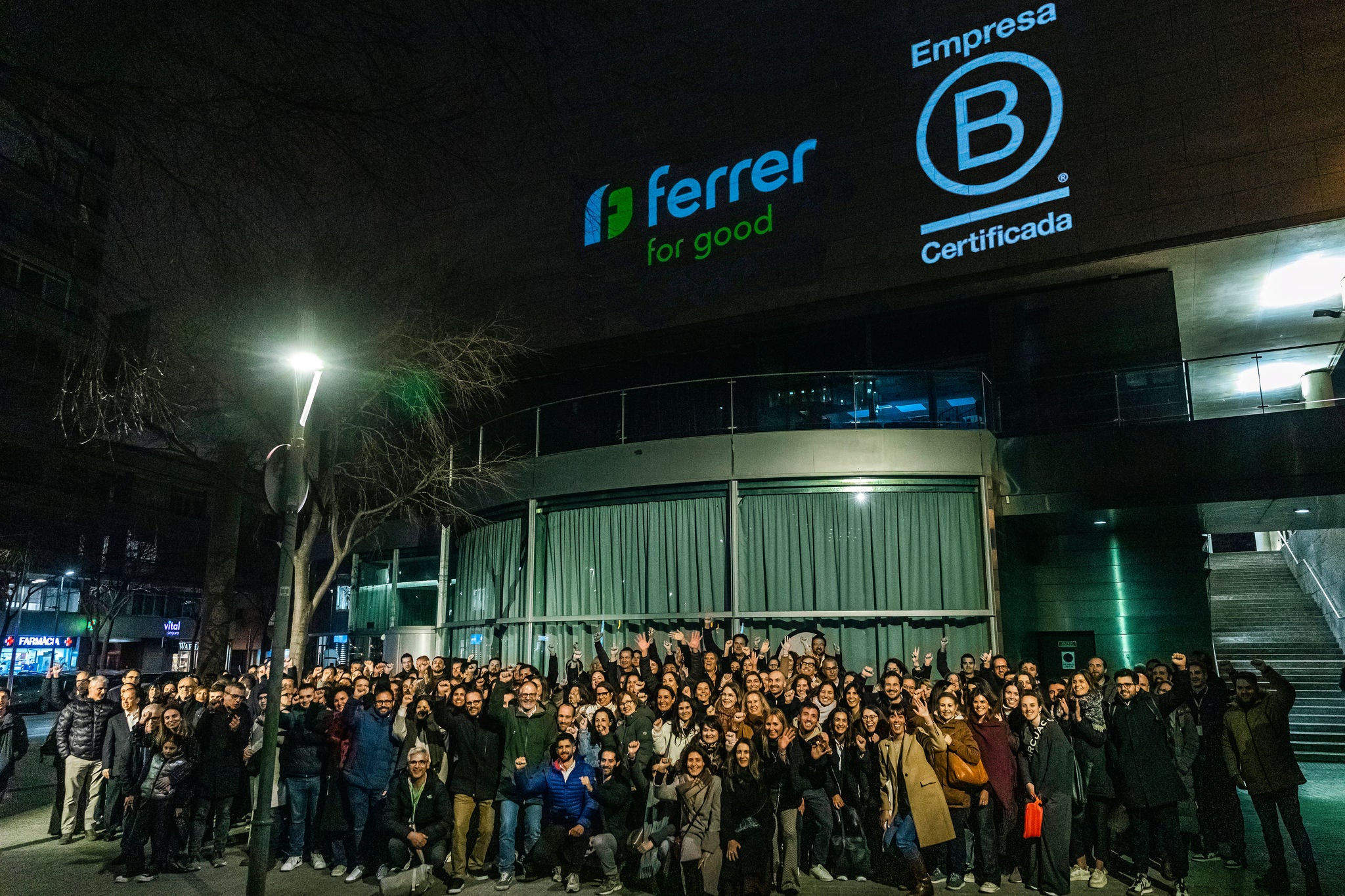 Grupo numeroso de personas posando de noche en el exterior de un edificio acristalado, en una imagen de ambiente corporativo y celebrativo.