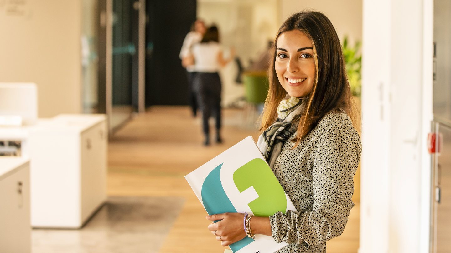 Empleada sonriente sosteniendo una carpeta corporativa con el logotipo del Grupo Ferrer en las oficinas de la empresa.