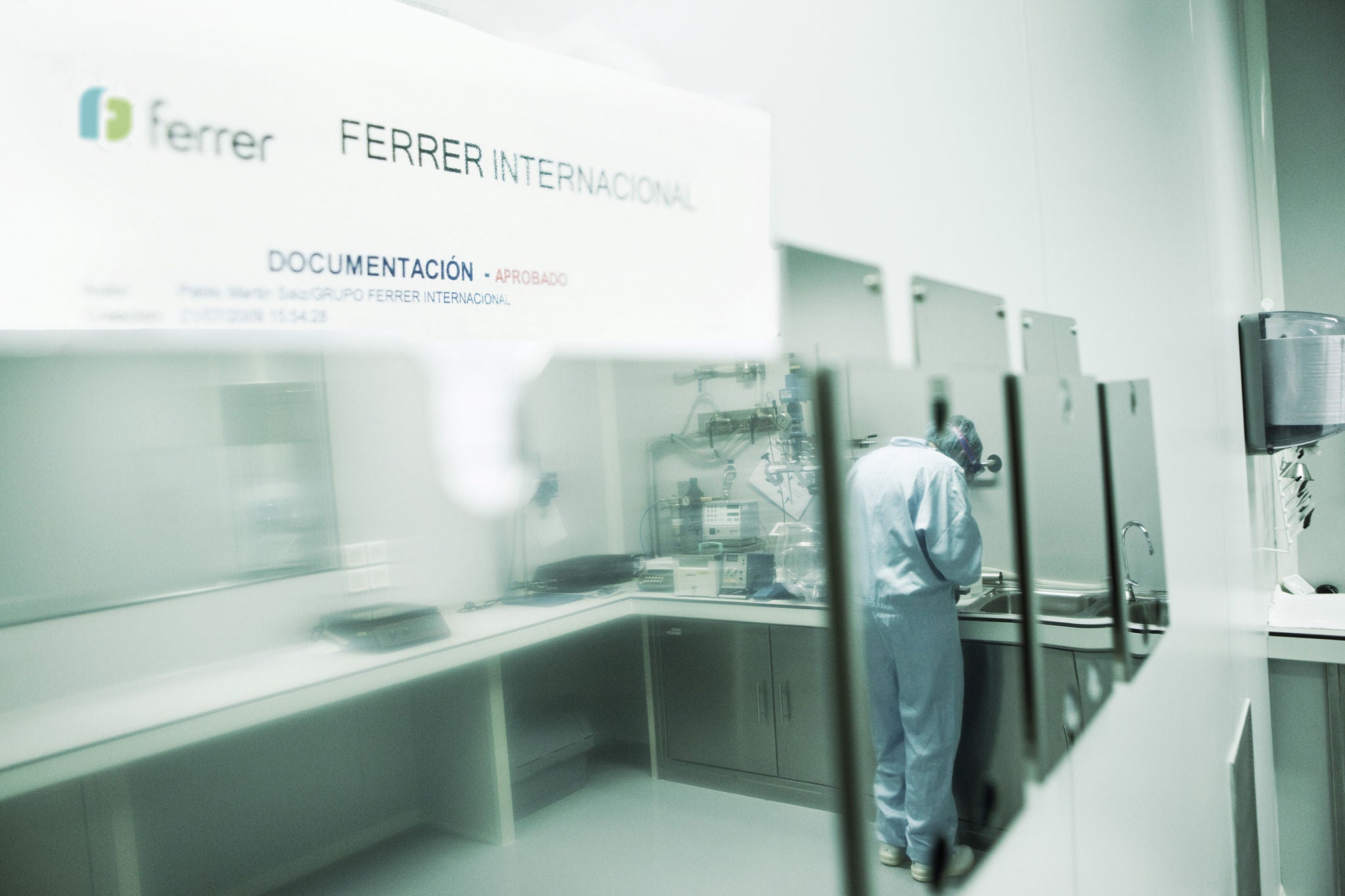Vista de un área de documentación en instalaciones de Ferrer Internacional, con una persona trabajando en un entorno técnico o de laboratorio tras una zona acristalada.