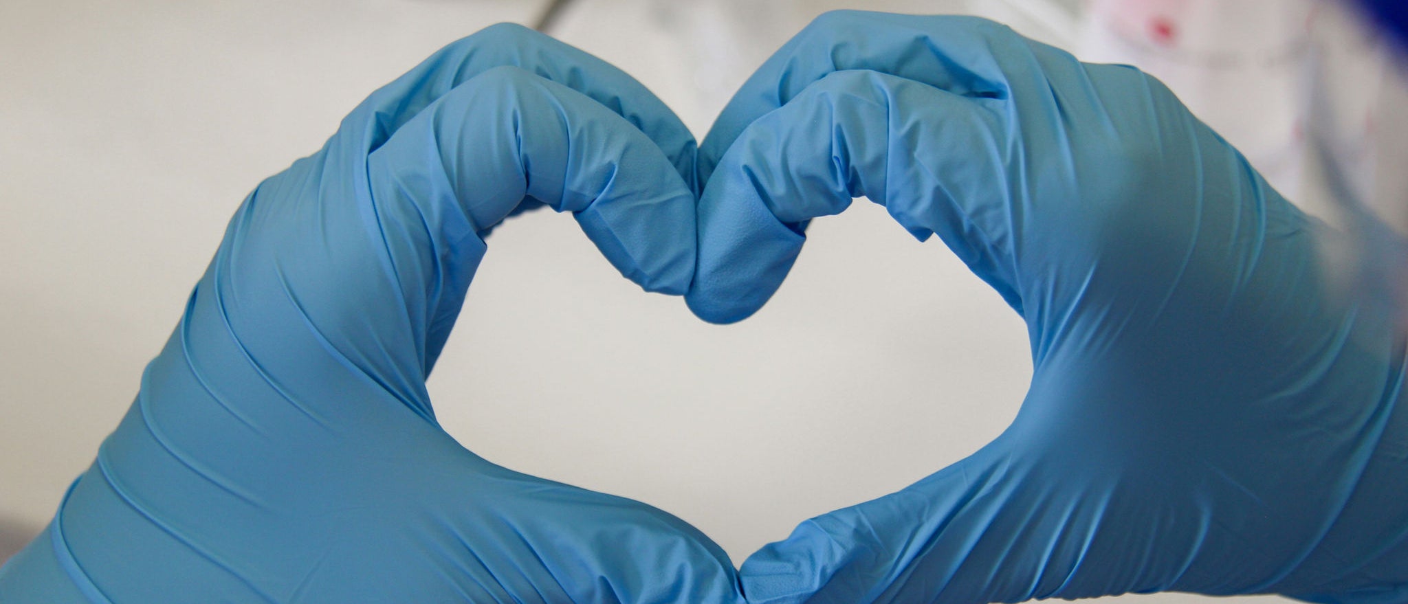Manos con guantes azules forman un corazón en un entorno de laboratorio, representando el compromiso de Ferrer con el cuidado, la ciencia y la salud.