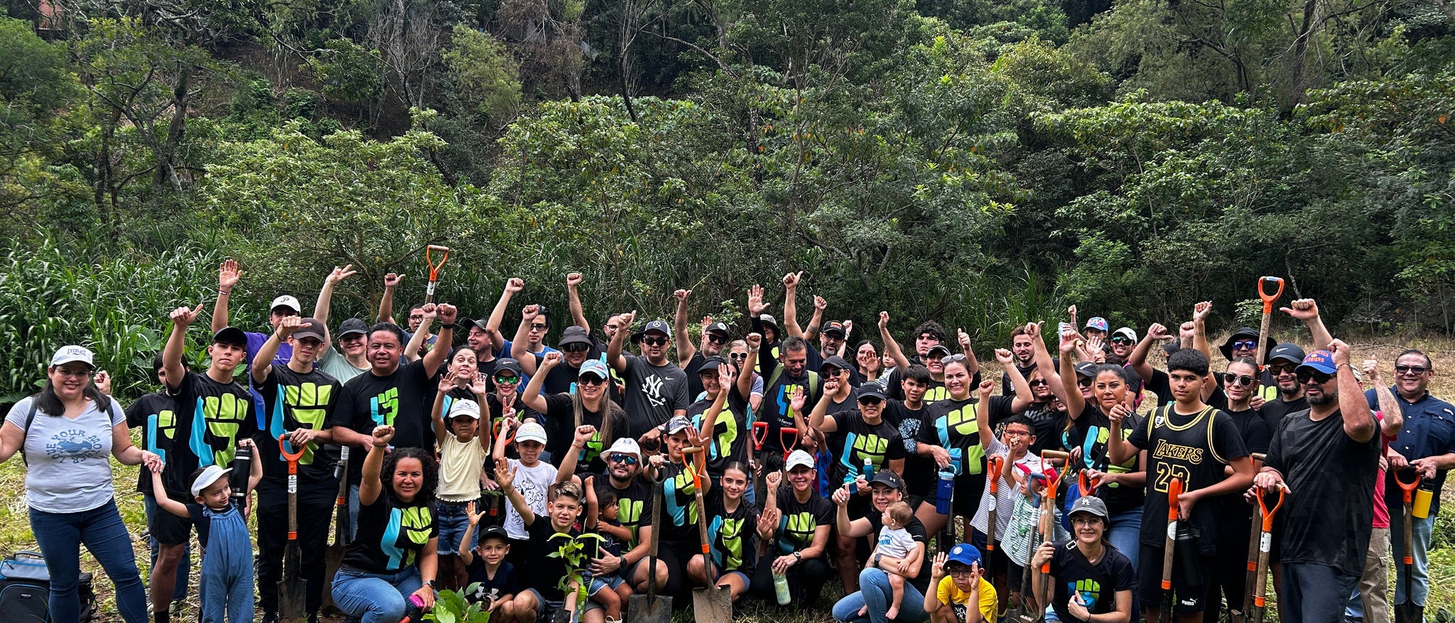 Ferrer volunteers pose in a group in a green and wooded area, with shovels and plants, celebrating a day of reforestation or environmental volunteering.