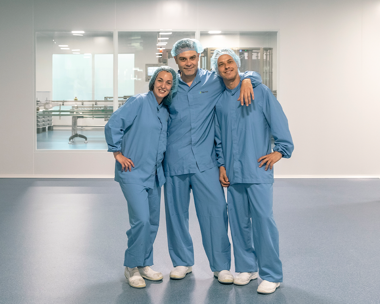 Equip de tres operaris amb vestits de protecció, reflectint el treball en equip, la cultura i els valors de Grup Ferrer en la seva planta de producció farmacèutica sostenible.