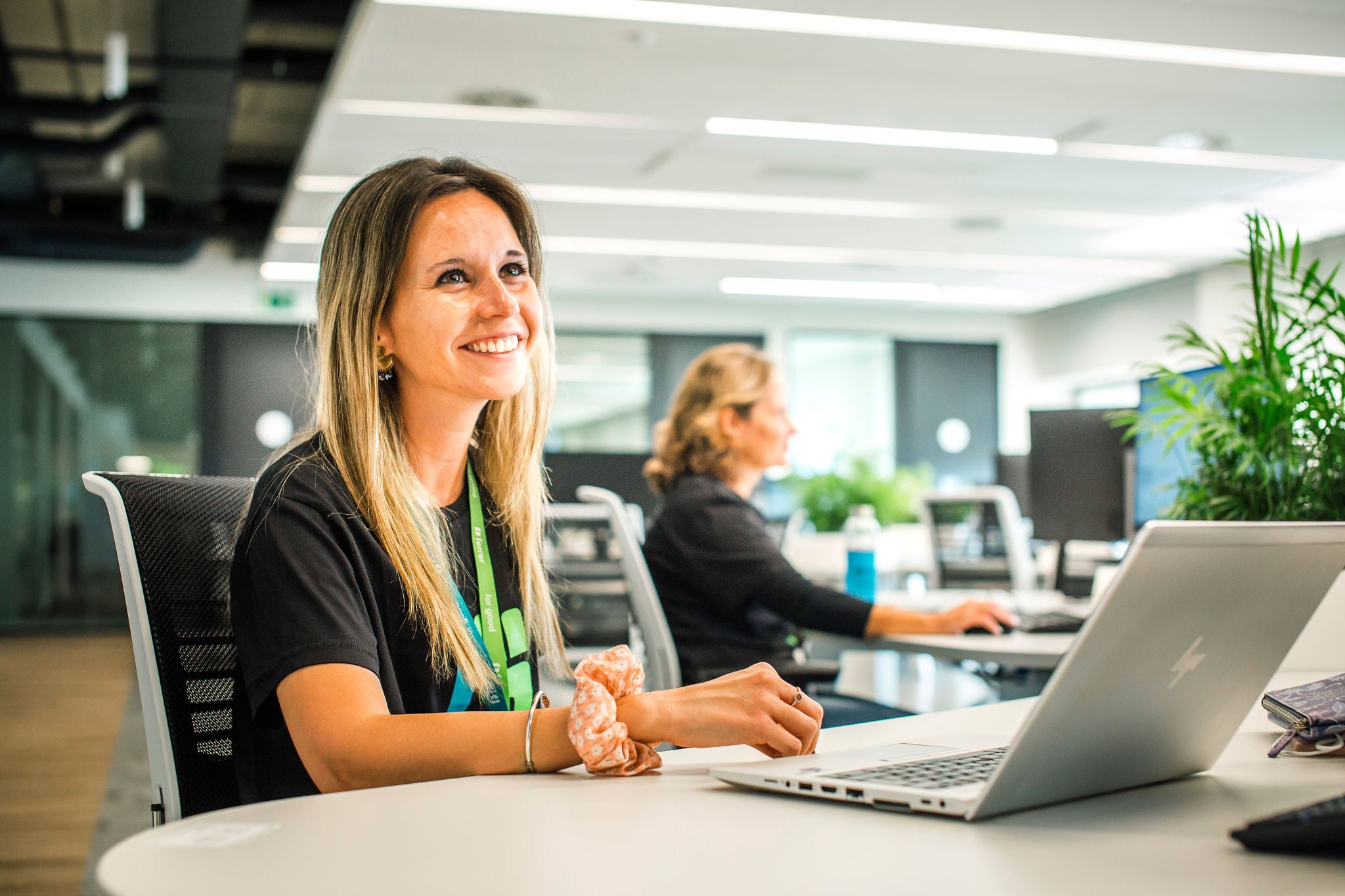 Ferrer's employee smiles as she works with a laptop in a modern, bright office, with another person in the background and a collaborative environment.