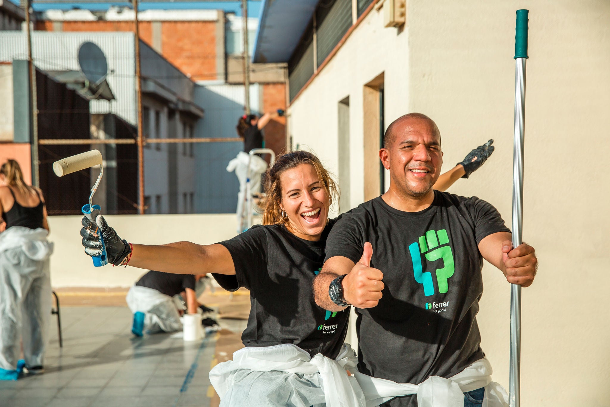 Dos voluntarios sonrientes con camisetas corporativas celebran mientras participan en una actividad comunitaria de pintura en una azotea.