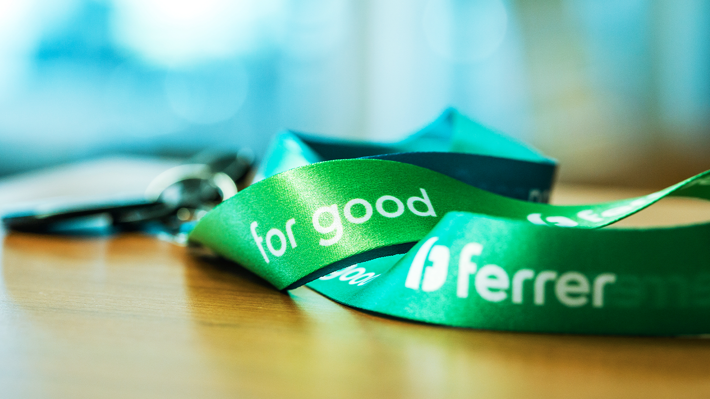 Primer plano de una cinta lanyards verde con los textos inscritos "for good" y "ferrer" sobre una superficie de madera lisa.