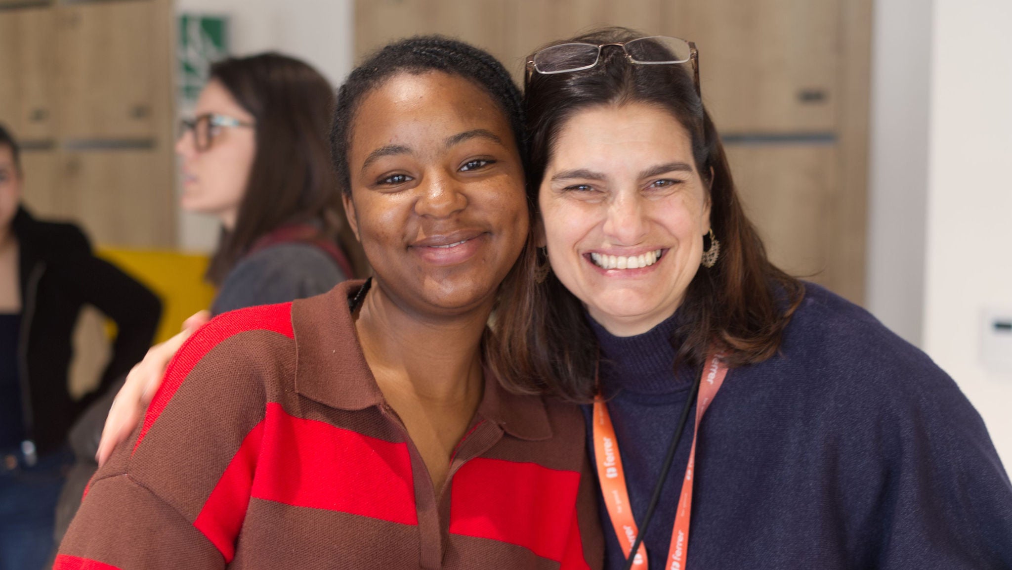 Dos mujeres sonrientes posan abrazadas en un espacio interior.