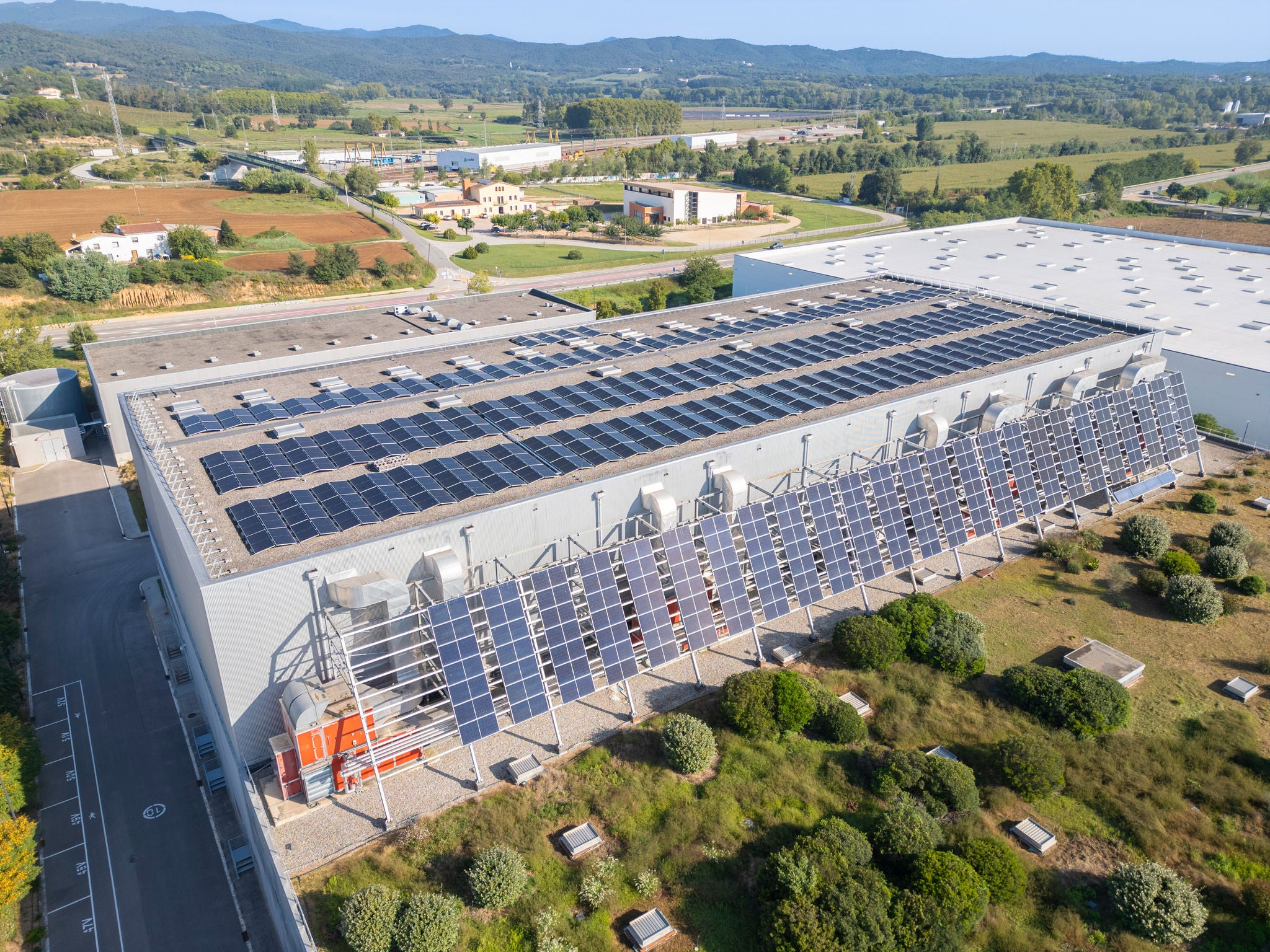 Vista aérea de una nave industrial con una gran instalación de paneles solares fotovoltaicos en el tejado y en la fachada lateral.