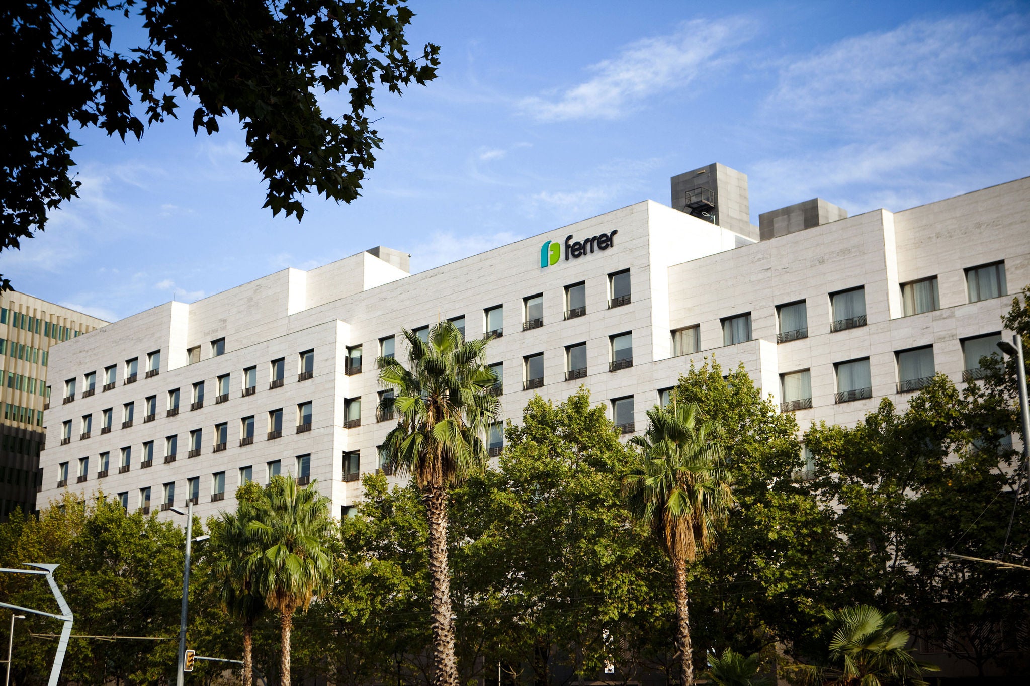 Edificio de Ferrer en Barcelona, con el logotipo de la compañía en la fachada y zonas verdes en primer plano.